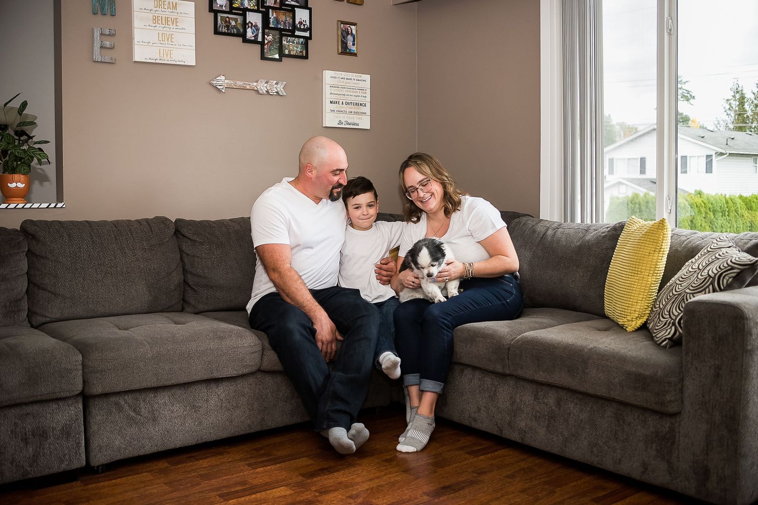 A family of three, plus their adorable dog, sit together on the couch during their at-home family photo session.