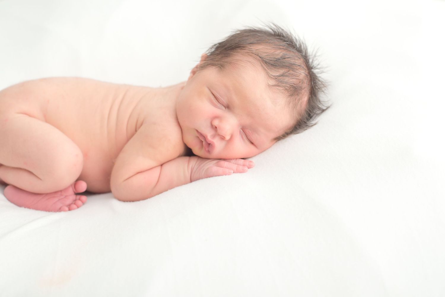 newborn baby boy resting on his hands and belly during a newborn studio session all white in Houston texas