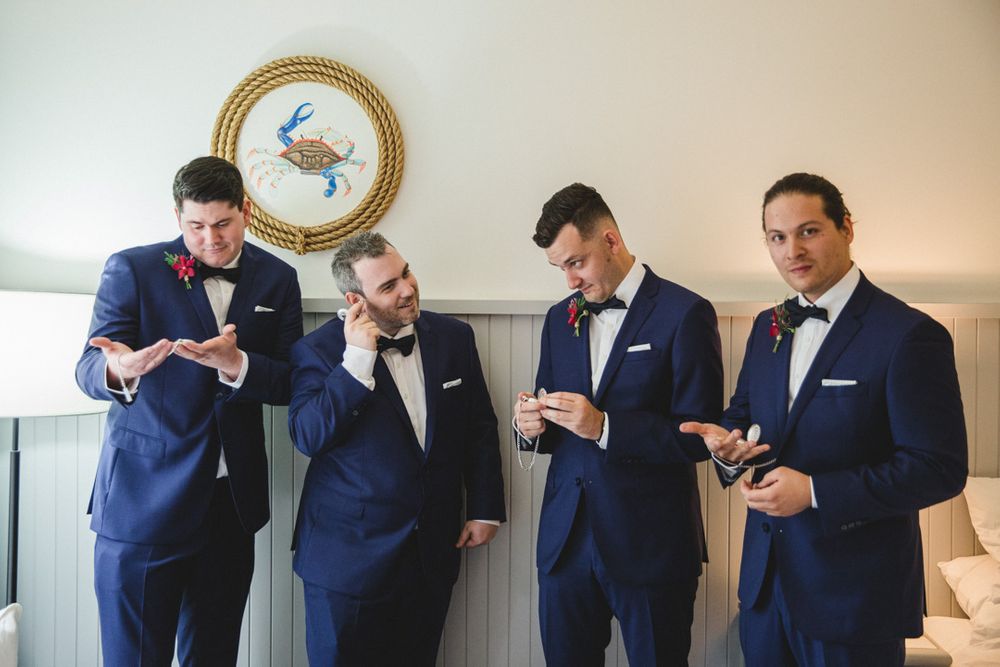 Wedding party in navy suits examining rings in an indoor setting.