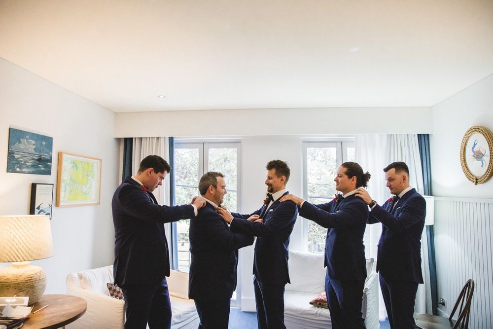 Wedding party lined up against white wall performing synchronized ring gestures.