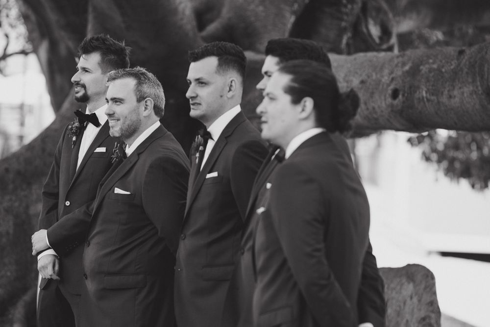 Groomsmen in dark suits standing in formal line outdoors.