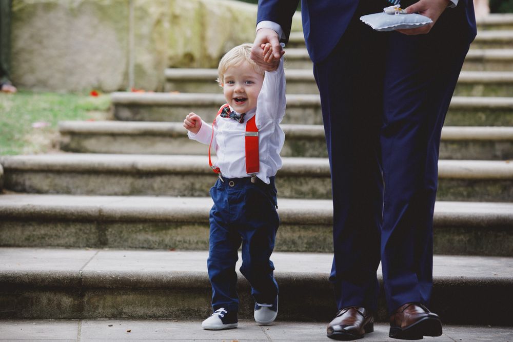A small child in suspenders and bow tie holds hands with an adult on stone steps.
