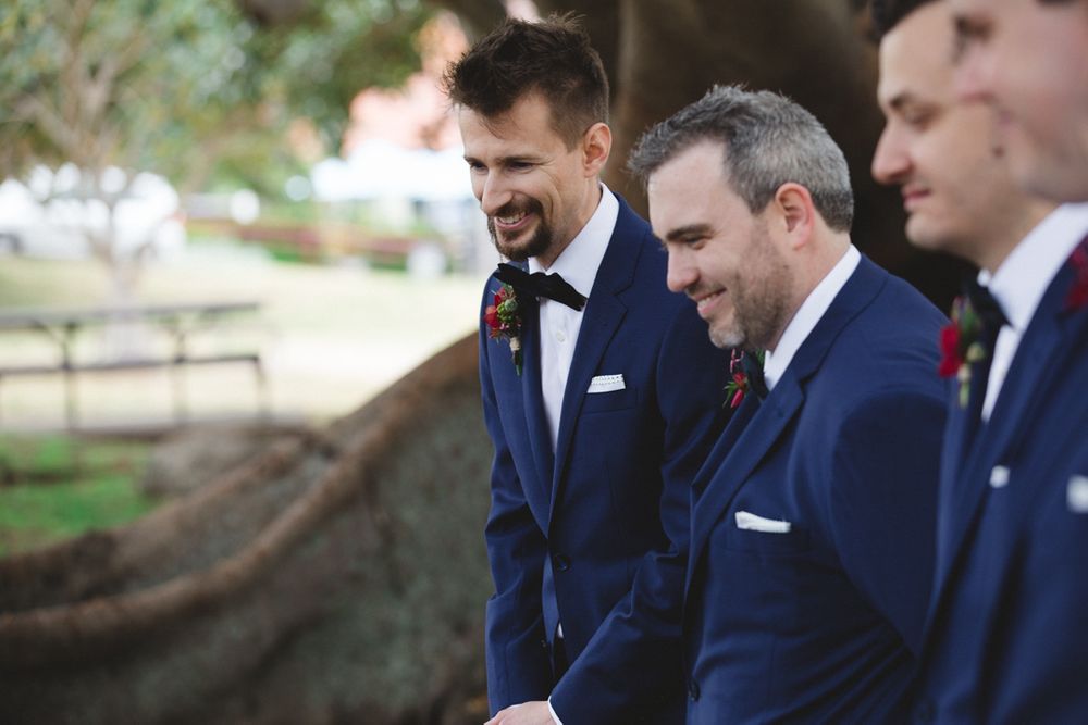 Groomsmen in navy suits share a laugh during an outdoor wedding.