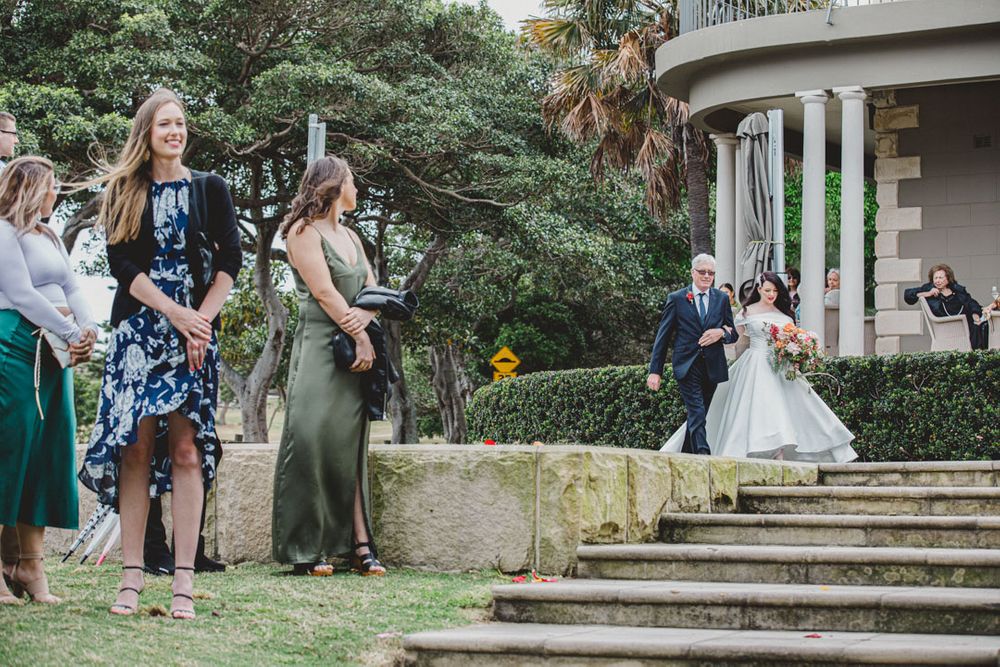 Wedding guests gather on garden steps while watching the ceremony.