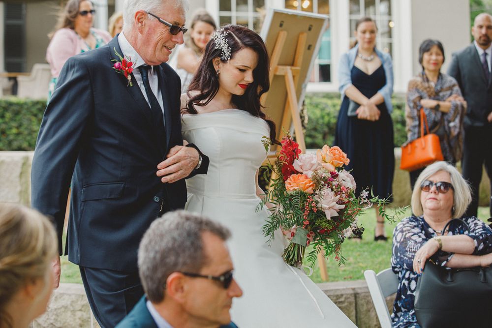 An outdoor wedding ceremony takes place on the steps of a historic building.