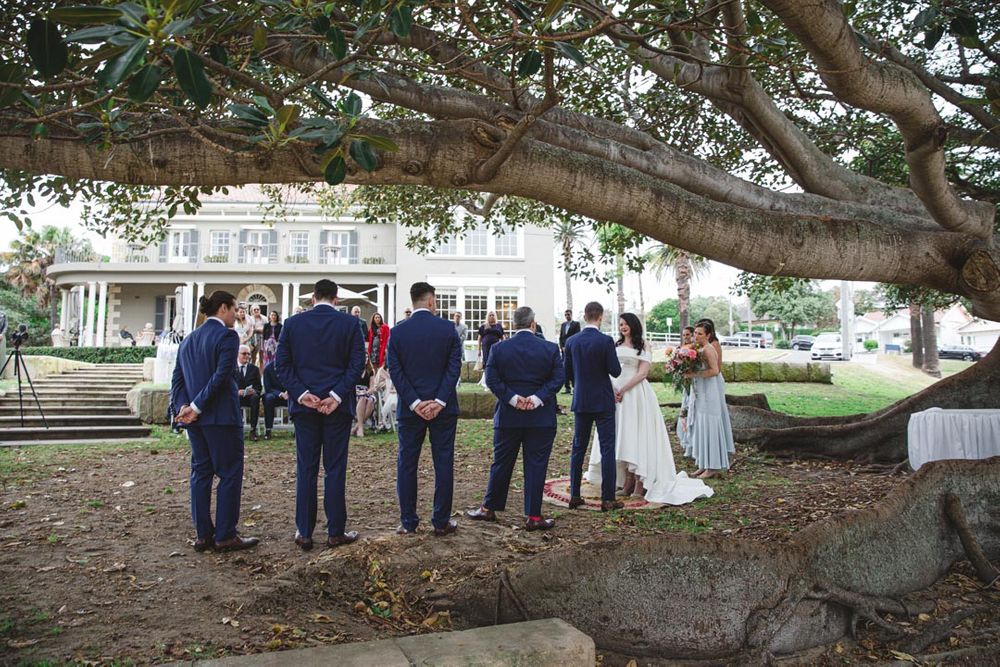 A wedding party poses under a large tree for formal photographs.