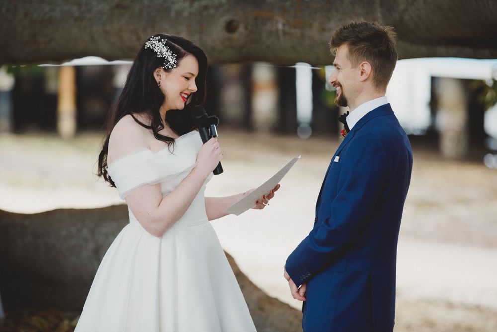 A couple shares a joyful moment while exchanging vows under a tree.