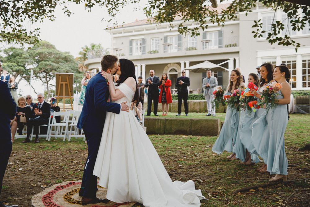 Wedding party poses outdoors with bridesmaids in light blue dresses and groomsmen in navy suits.