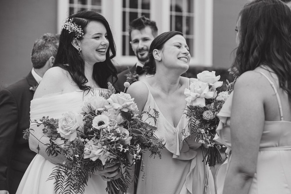 Wedding party shares joyful laughter while holding bouquets during outdoor celebration.