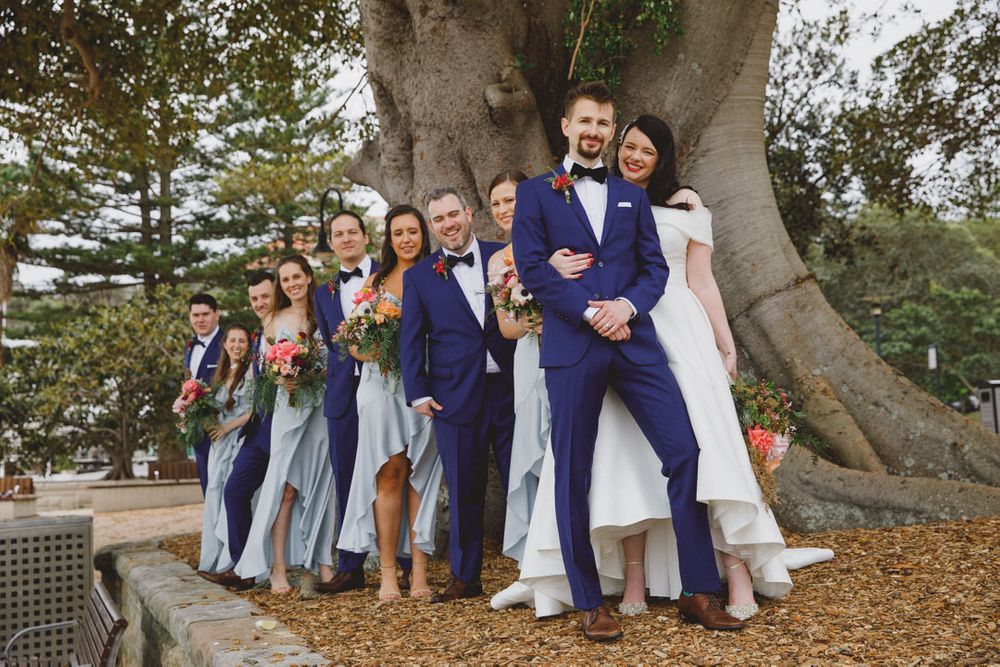 Group photo session under a majestic tree with wedding party in blue and navy attire.