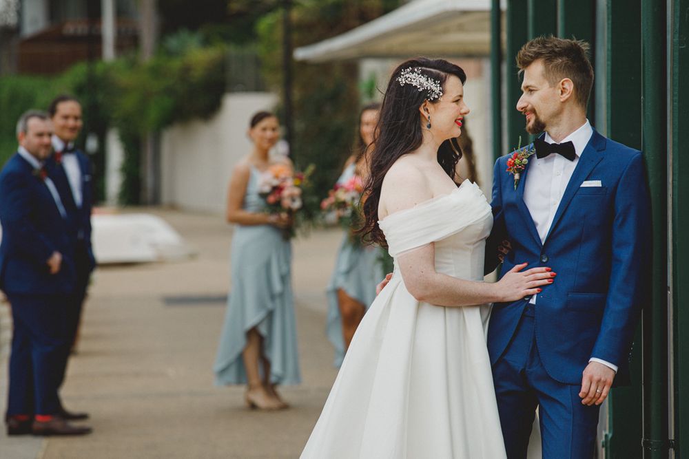 Wedding party walking along green pathway with couple in white dress and navy suit.