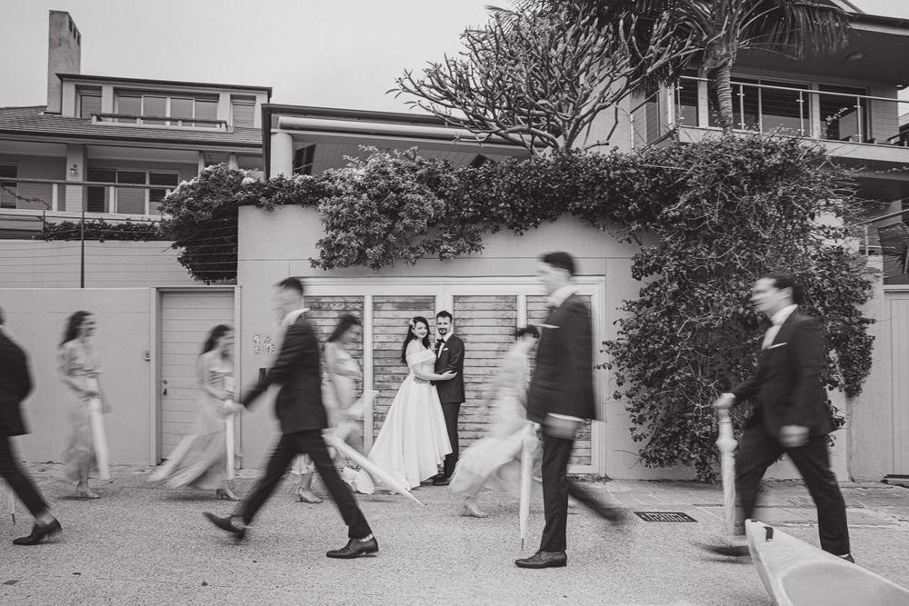 Black and white photo of wedding party members walking in synchronized steps with umbrellas.