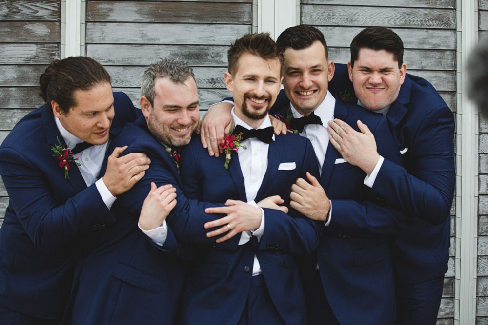 Groomsmen in navy suits sharing a candid moment together outdoors.