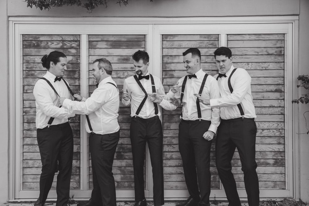 Wedding party members lined up against rustic wooden wall in formal attire.
