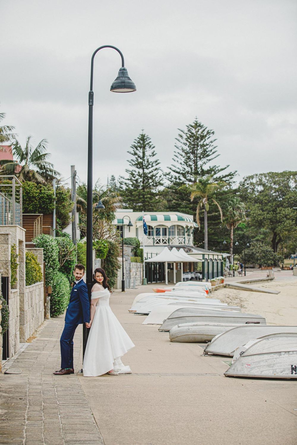 Coastal boardwalk with lamp posts and upturned boats along the shoreline.