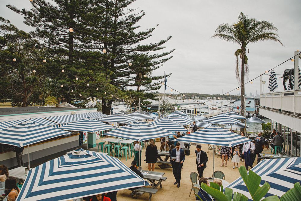 Blue and white striped umbrellas line a beachfront venue with palm trees and ocean views.