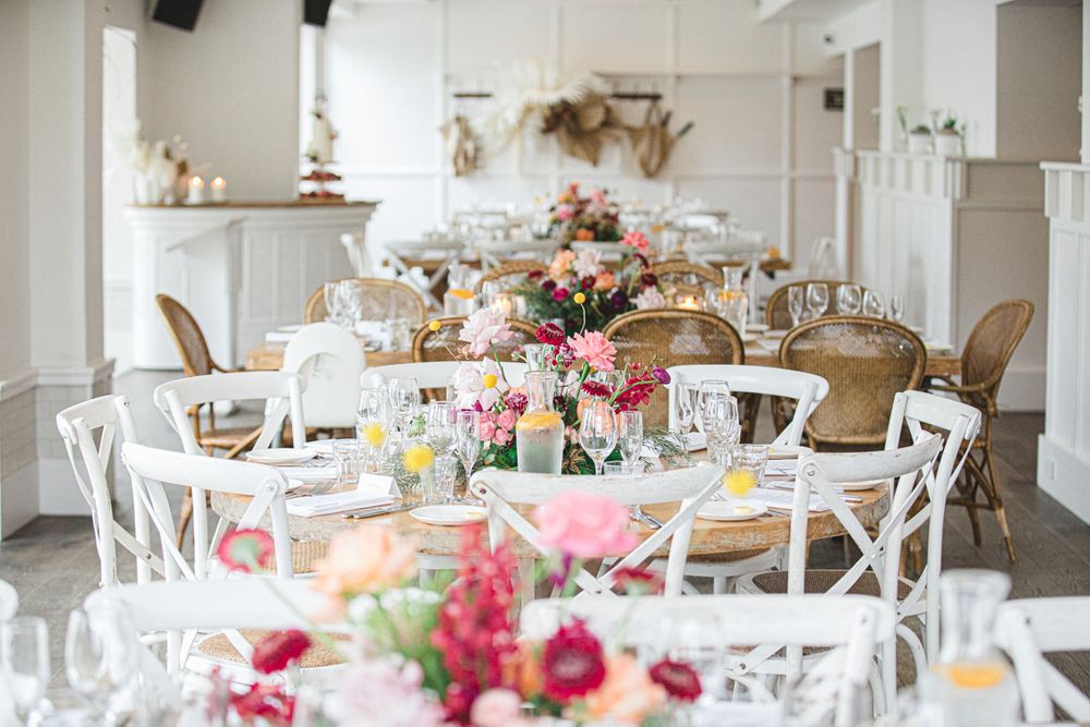 Elegant white reception tables decorated with pink floral centerpieces in a bright coastal venue.