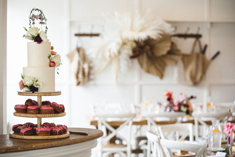 Wedding dessert display with tiered cake stands and floral decorations on white tablecloths.