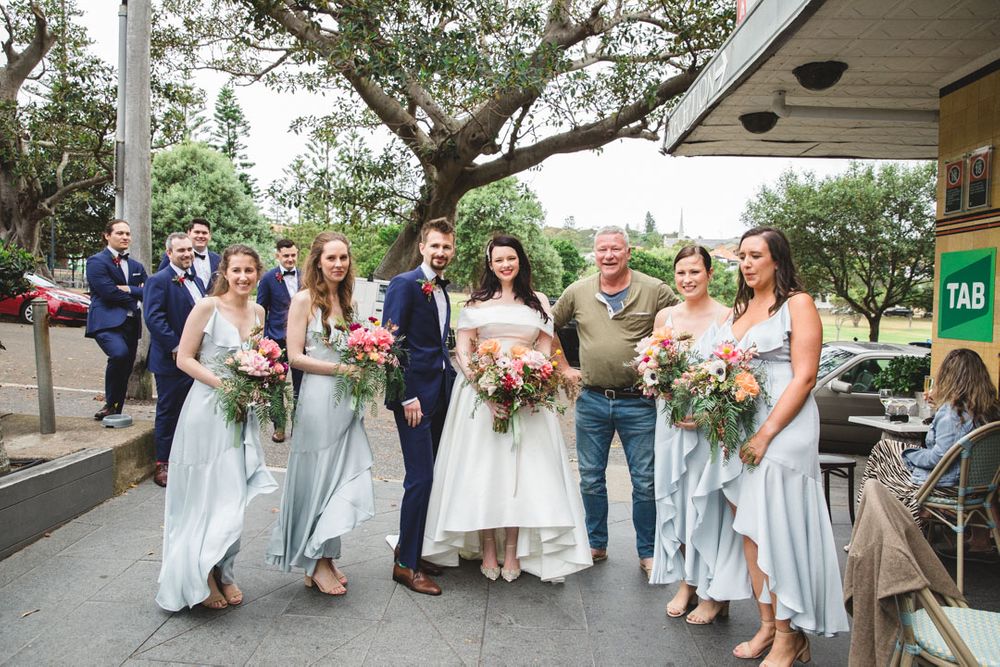 Wedding party gathered on a covered outdoor patio with lush greenery in the background.