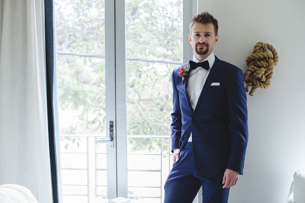 A person in a navy blue suit and bowtie poses by a bright window.