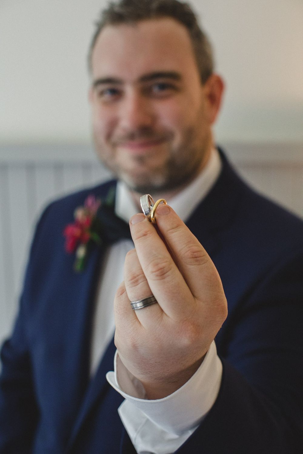 Close-up shot of groom's hands holding a wedding ring against a navy suit backdrop.