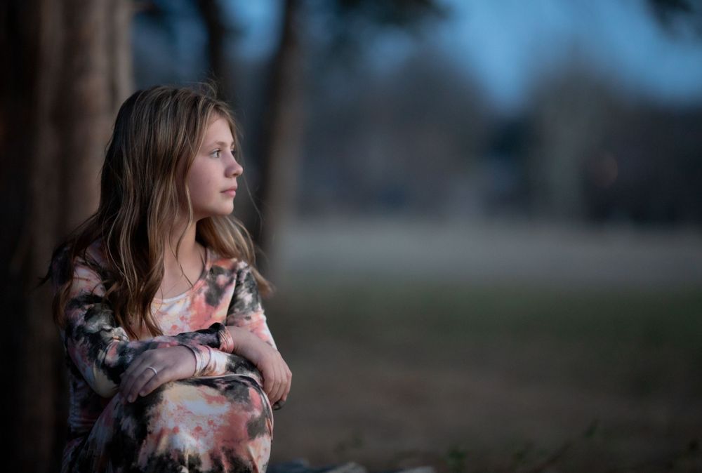 High school senior looking into the distance under a tree at dusk during a senior session near Mountain Home, Arkansas