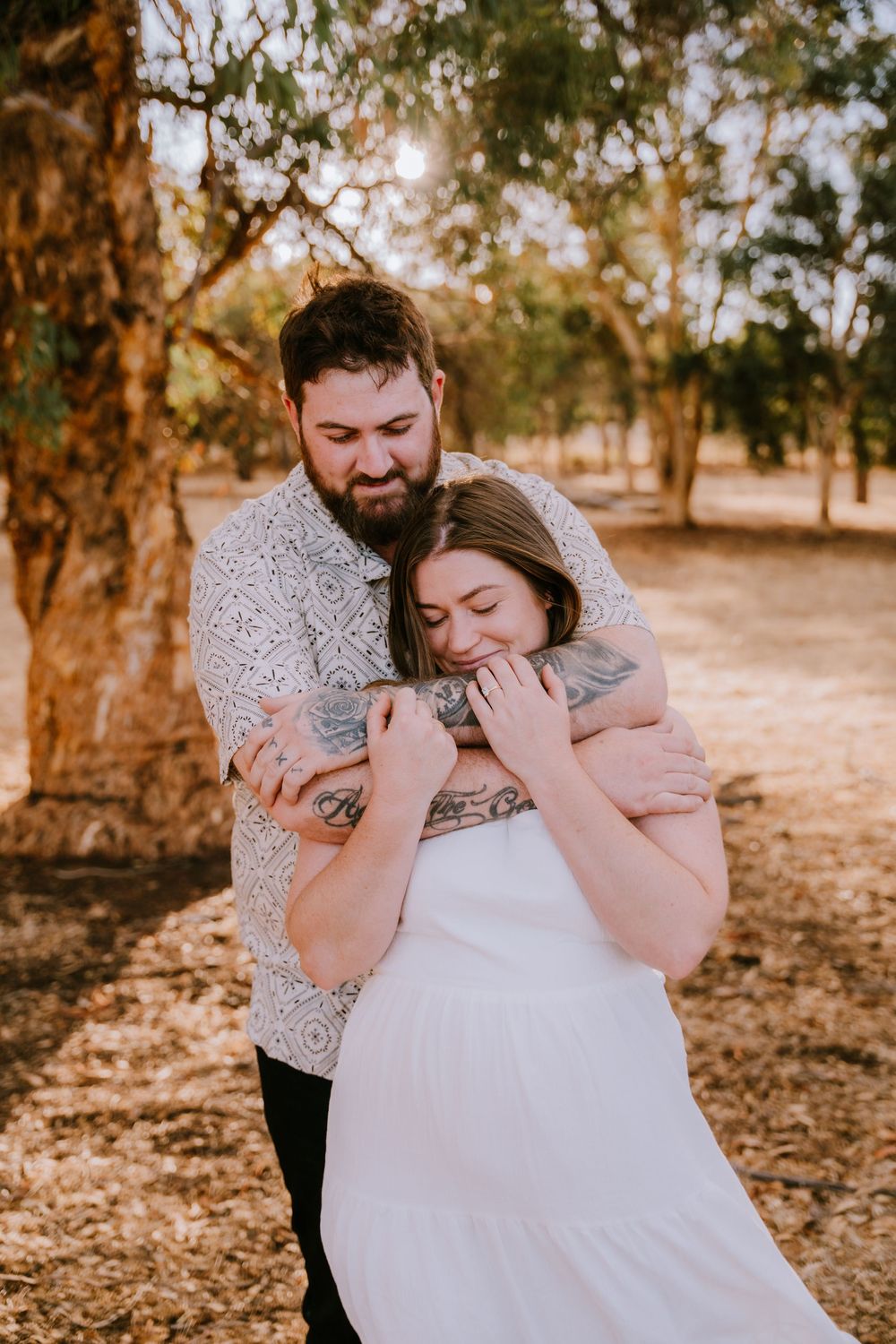 A couple shares an intimate moment outdoors among trees during a photo session.