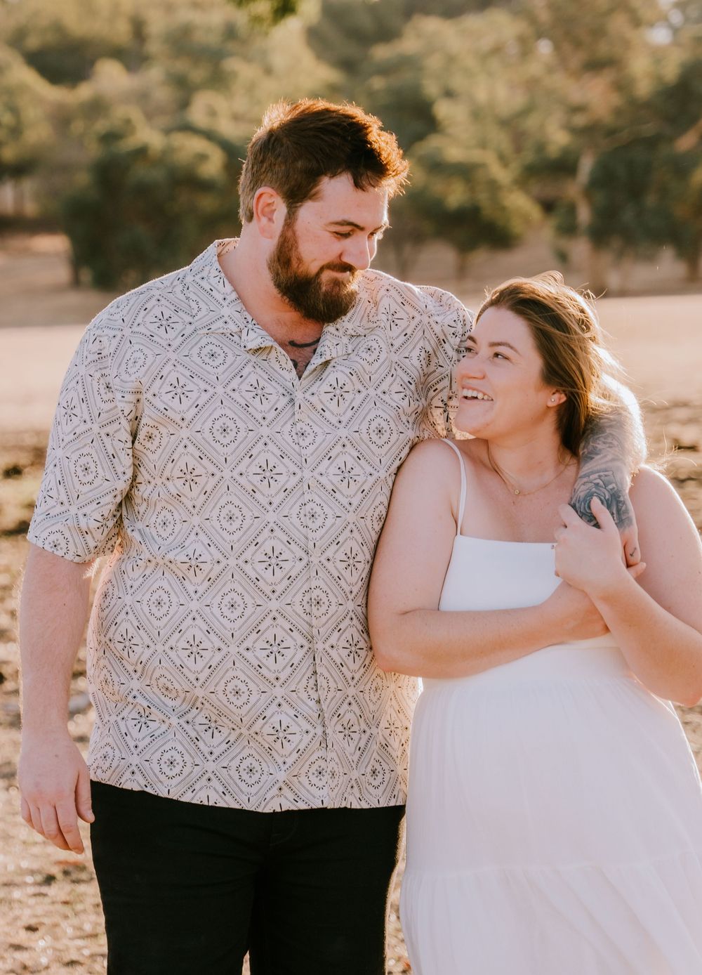 A couple in casual attire shares playful moments during a sunset photo session.