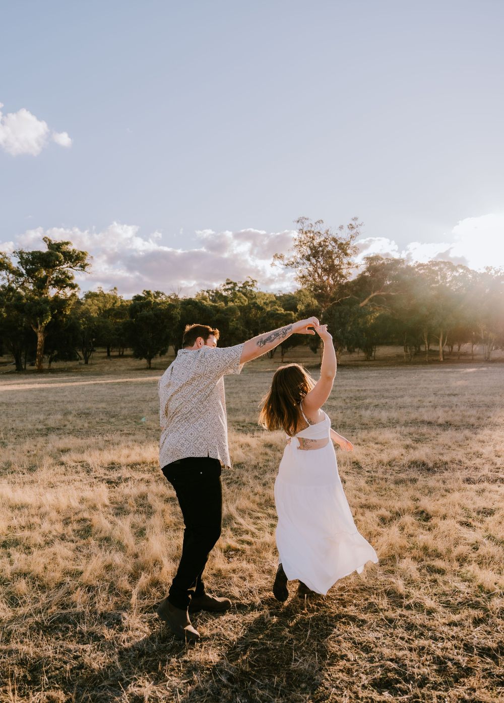 A couple dances together in a golden field during sunset.