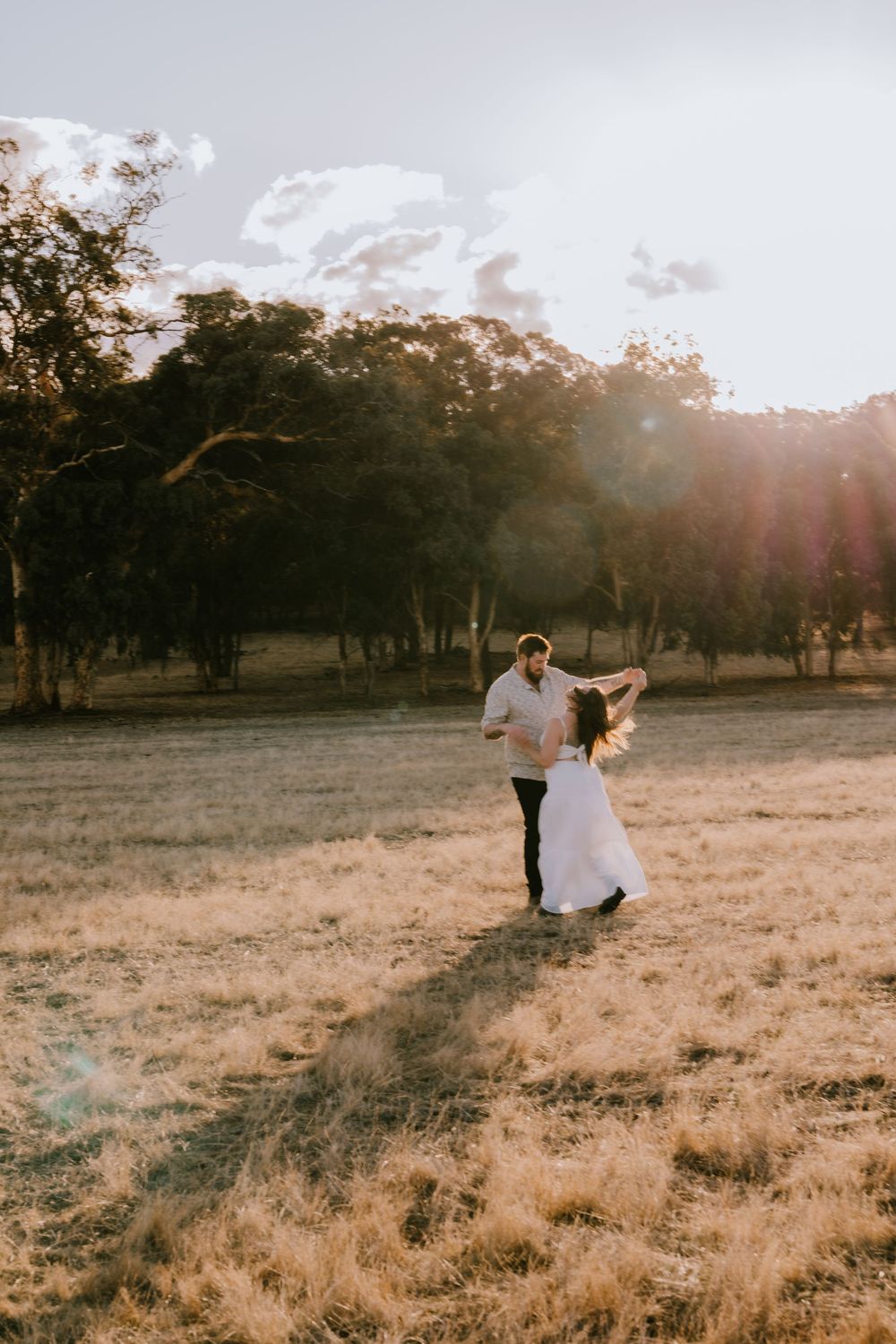 A couple shares a romantic dance in a rustic field at dusk.