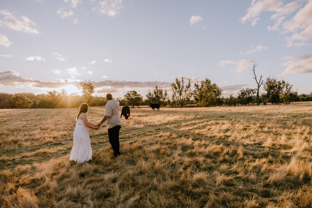A couple walks together across a grassy field during golden hour.