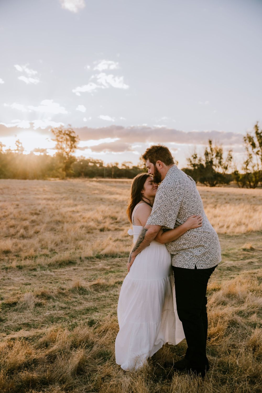 A romantic couple embraces in a sunlit field during golden hour.