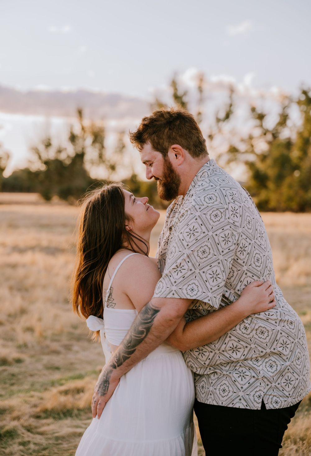 A couple shares an intimate embrace in a field during sunset.