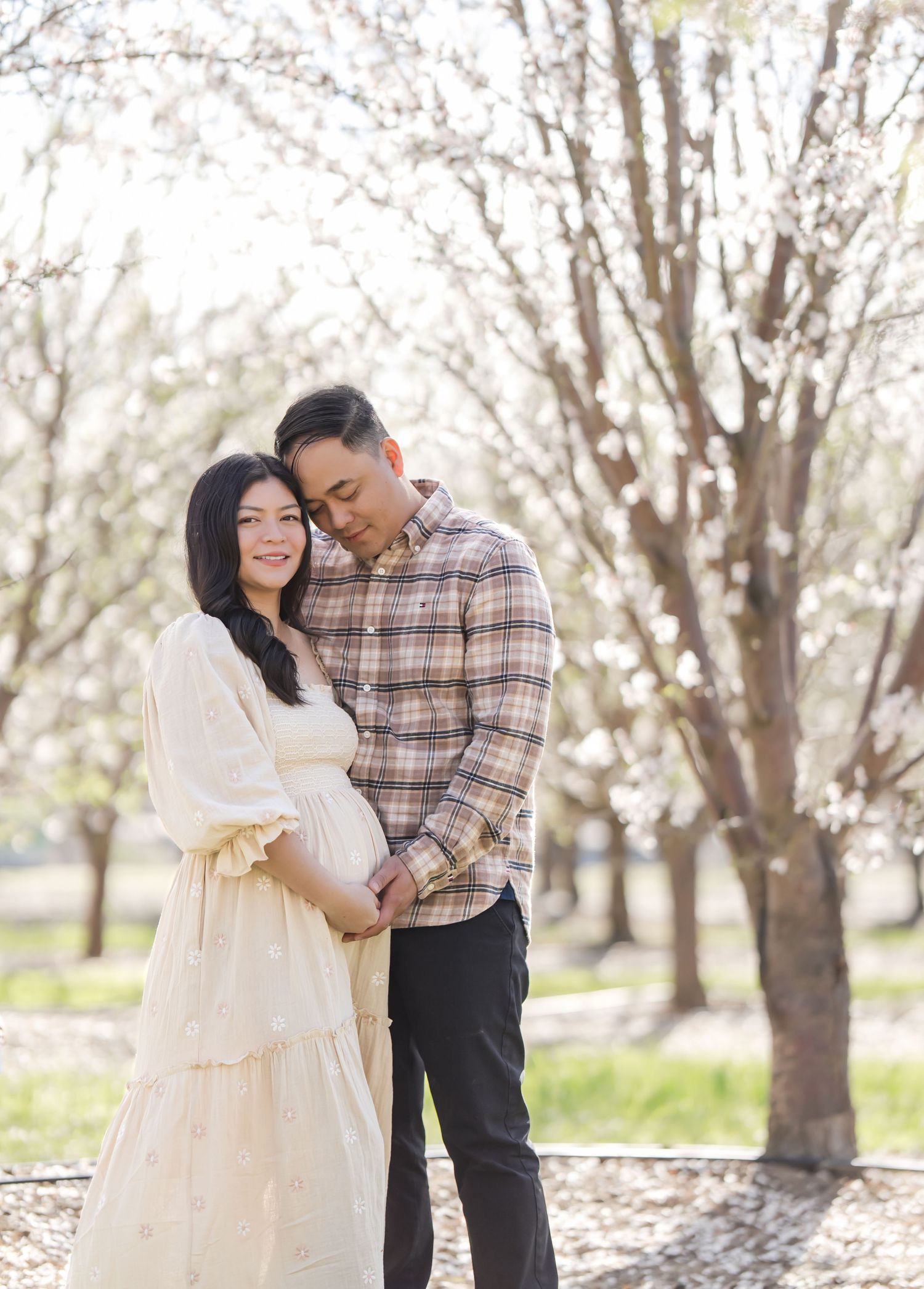 Close-up of a glowing mother-to-be standing among the cherry blossoms, her hands gently cradling her belly, celebrating the anticipation of