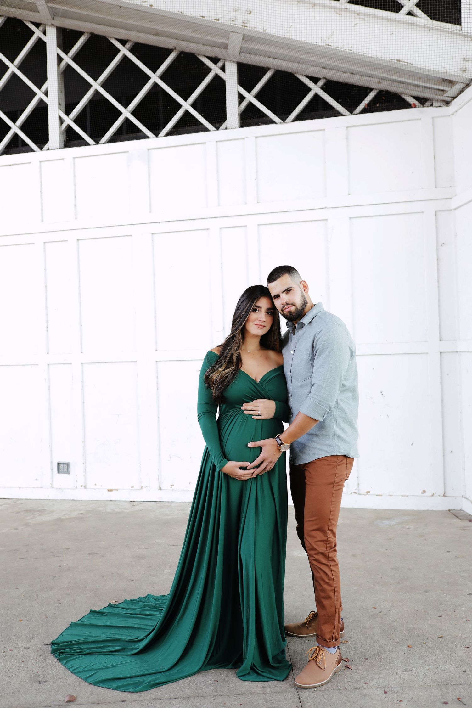 Pregnant woman in emerald green gown with partner in maternity portrait outdoors.