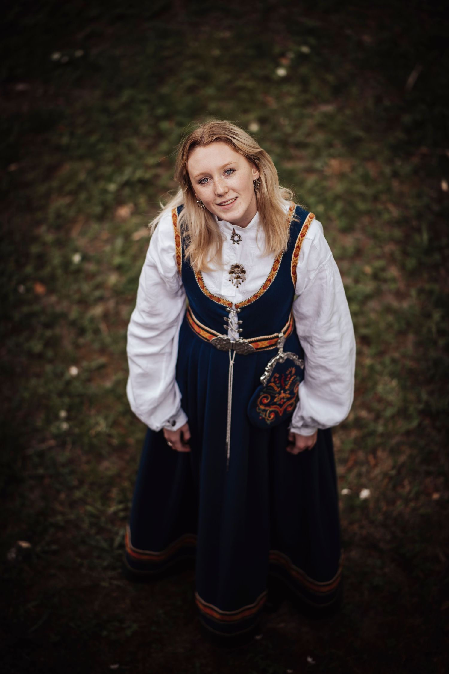 Dark blue traditional Nordic dress with embroidered details and white blouse photographed in moody outdoor setting.
