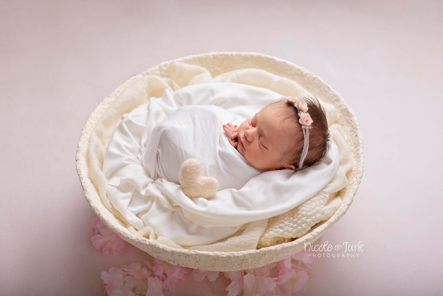 newborn baby girl wrapped in white in handcrafted white bowl with white heart and pink flowers