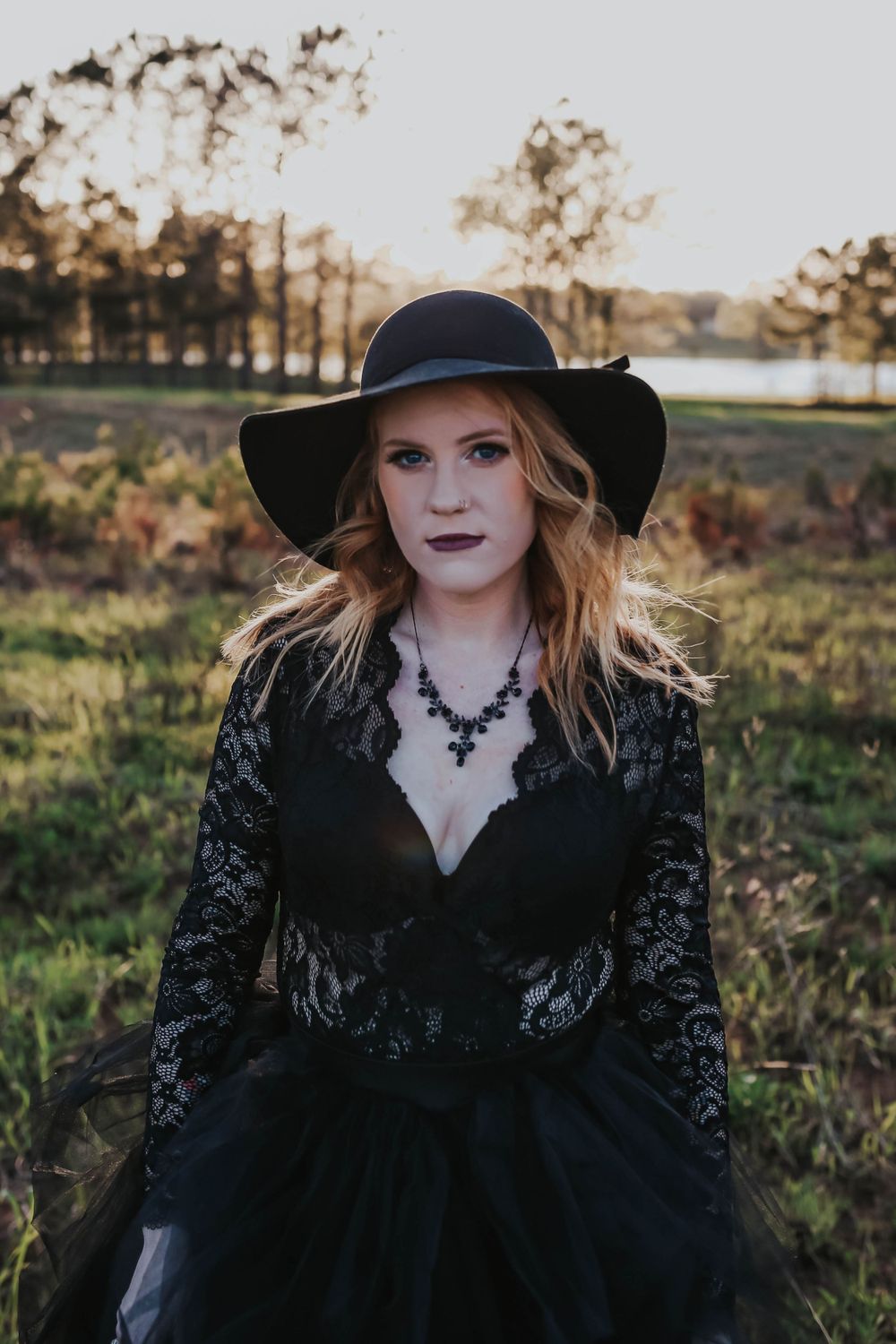 Gothic-inspired portrait featuring black lace dress and wide-brim hat in natural setting.