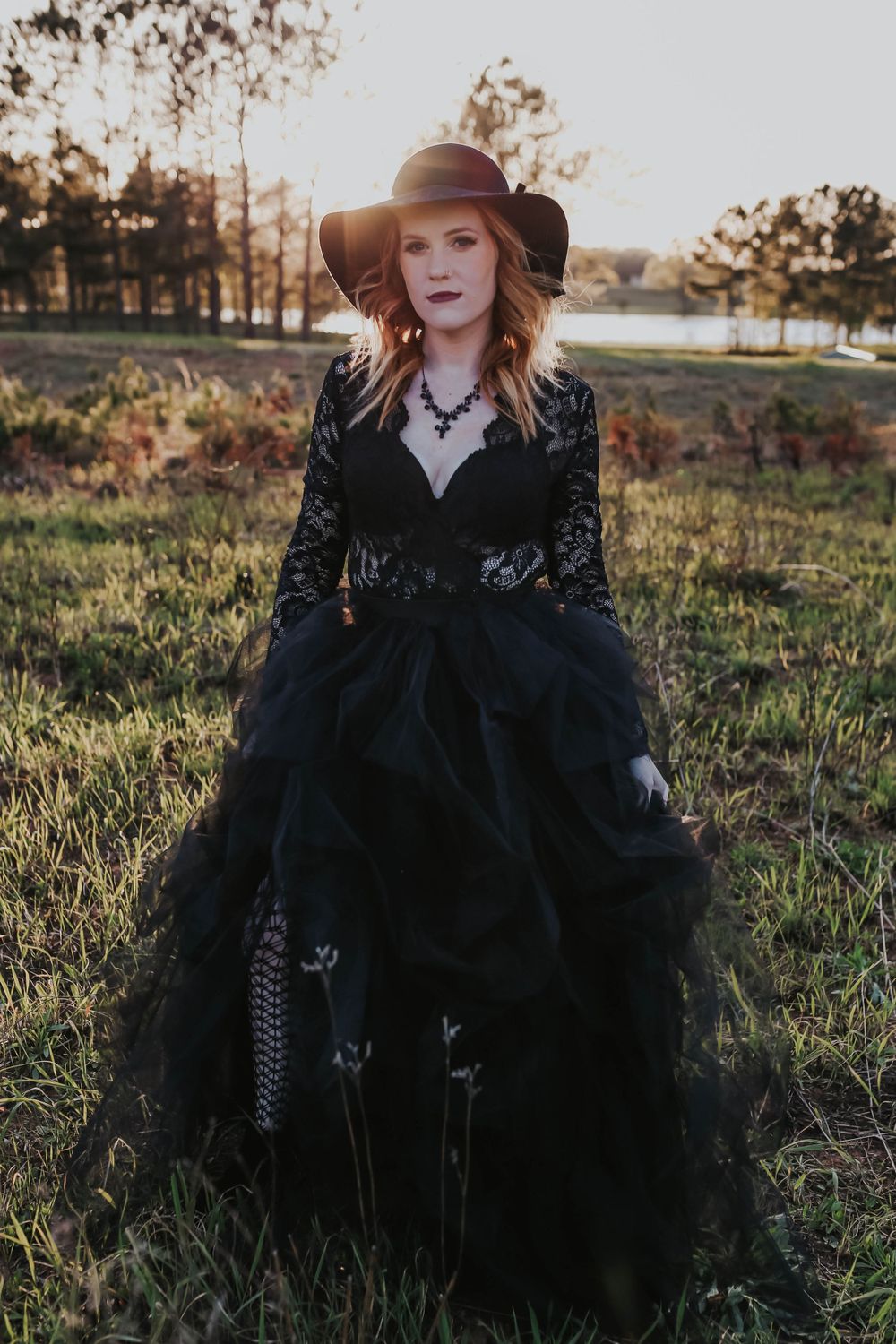 Artistic portrait in gothic black dress sitting in autumn field.