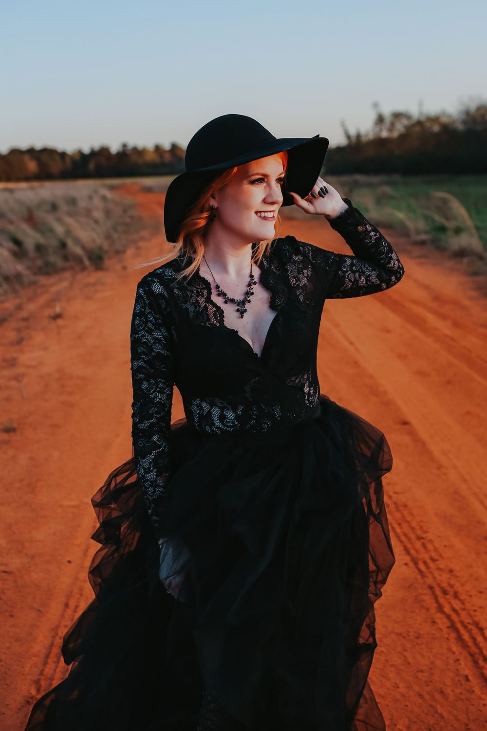 Dramatic fashion portrait on red dirt road wearing black lace dress and wide-brim hat.