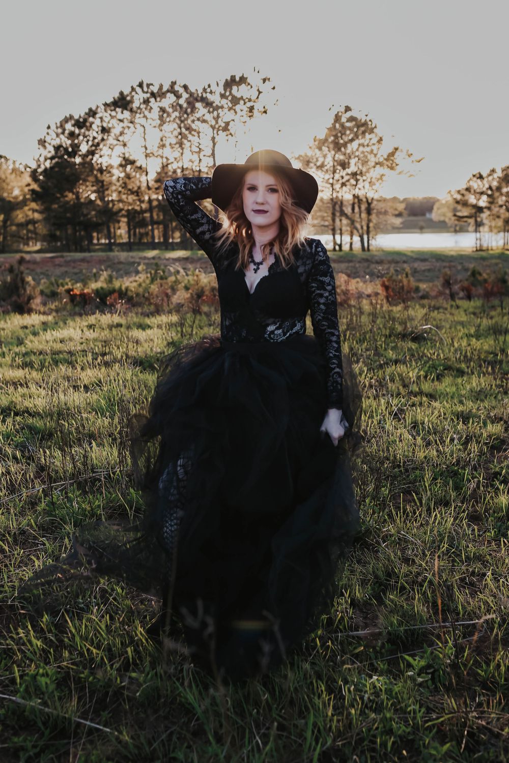 Dramatic outdoor portrait in flowing black dress against sunset landscape.