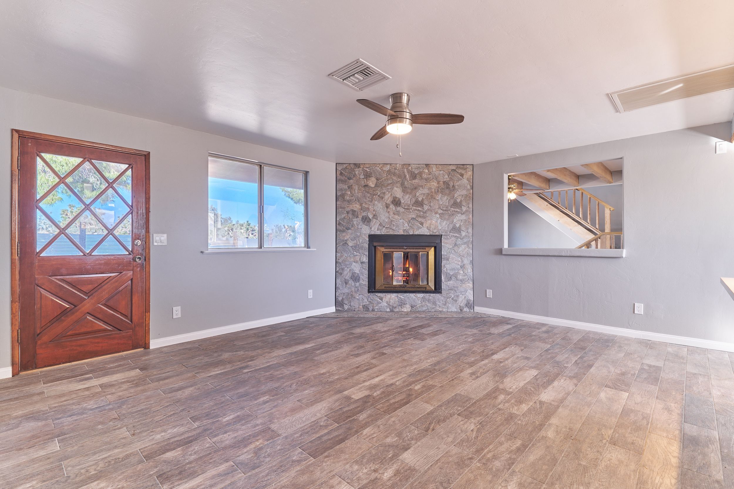 Empty living room featuring corner fireplace, wooden door, and gray stone accent wall.