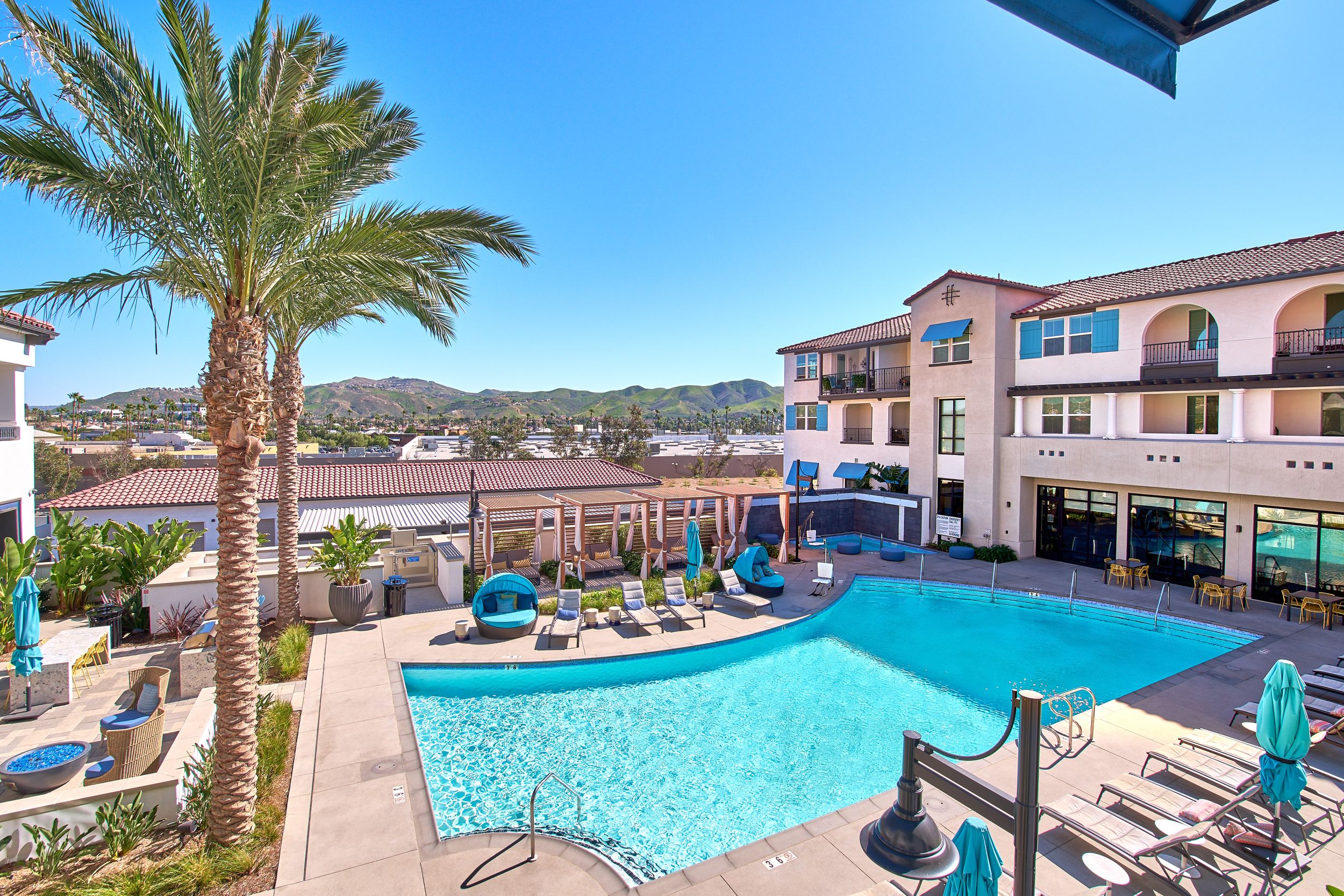 Resort-style pool area with palm trees, loungers, and Mediterranean-style architecture.