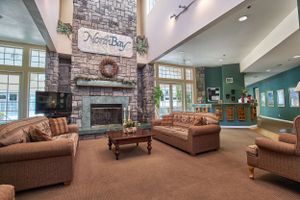 Cozy community room features stone fireplace, brown leather furniture, and high vaulted ceilings with natural lighting.