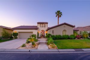 Mediterranean style home exterior at dusk with desert landscaping and palm trees.