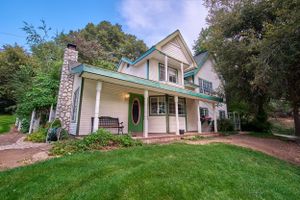 Elegant two-story craftsman style home with stone accents and wrap-around porch surrounded by lush landscaping.