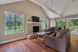 Living room with stone fireplace, vaulted ceiling, and large windows offering natural light.