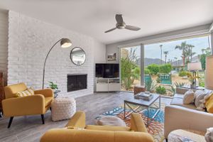 Contemporary living area with white brick fireplace, yellow accent chairs, and large windows overlooking greenery.