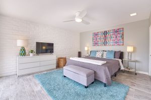 Modern bedroom with white brick wall, gray bedding, and turquoise area rug on light wood floors.