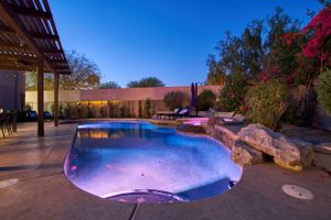 Illuminated pool with rock features and purple lighting creates a stunning twilight ambiance.